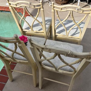 May include: Four bamboo-style chairs with light beige frames and patterned seat cushions. The chairs have a decorative back design. A pink flower sits on one chair. The chairs are outdoors near a pool.