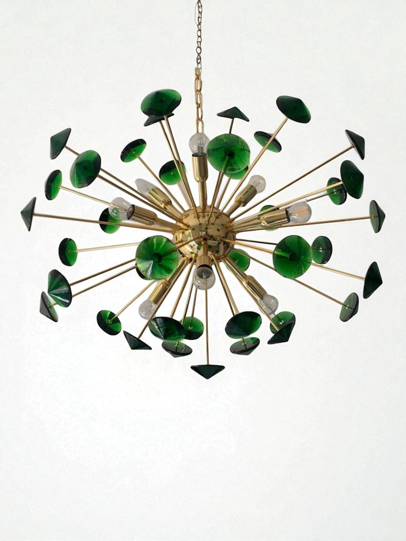 May include: A mid-century modern chandelier with a gold-toned metal frame. The fixture features multiple light bulbs and is adorned with green glass accents in various shapes, including discs and triangles. The chandelier hangs from a chain.