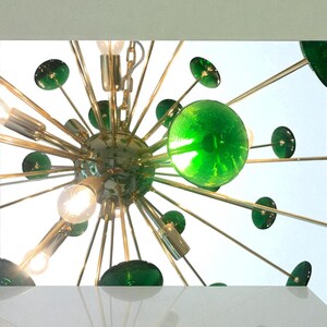 May include: A mid-century modern chandelier with a starburst design. The fixture features multiple light bulbs, green glass spheres, and gold-toned metal arms. The design is reminiscent of atomic age decor.