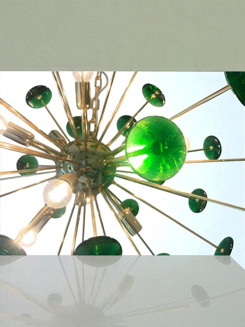 May include: A mid-century modern chandelier with a starburst design. The fixture features multiple light bulbs, green glass spheres, and gold-toned metal arms. The design is reminiscent of atomic age decor.