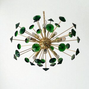 May include: A mid-century modern chandelier with a brass finish and green glass accents. The fixture features multiple arms extending from a central sphere, each holding a light bulb and decorative glass elements. The design is reminiscent of a starburst.
