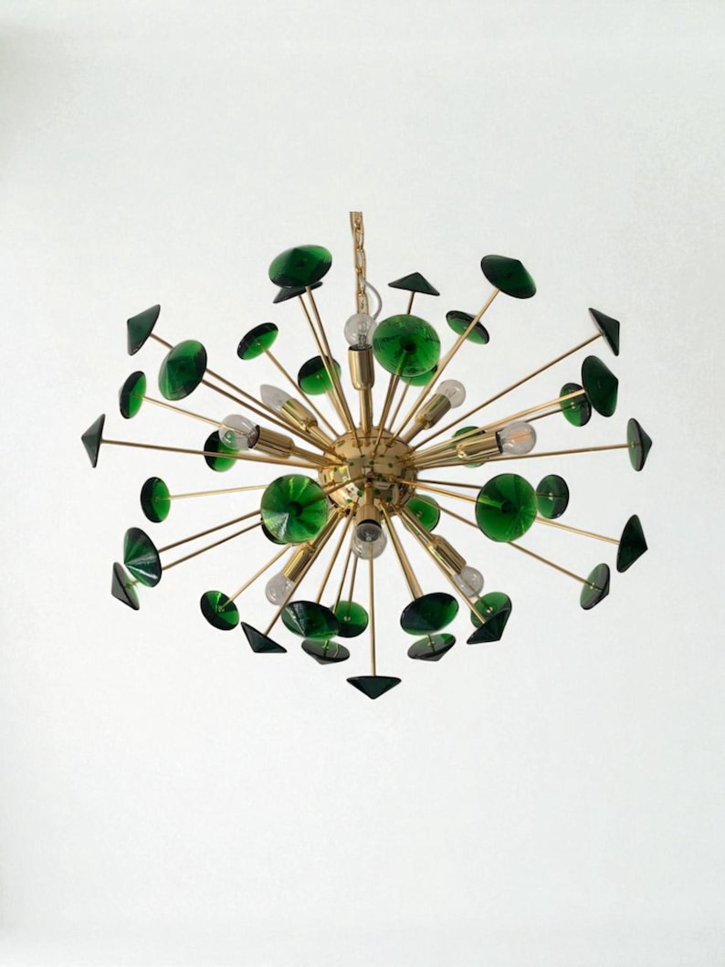 May include: A mid-century modern chandelier with a brass finish and green glass accents. The fixture features multiple arms extending from a central sphere, each holding a light bulb and decorative glass elements. The design is reminiscent of a starburst.