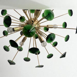 May include: A mid-century modern chandelier with a brass finish and dark green glass accents. The light fixture features multiple arms extending from a central sphere, each holding a green glass disc or sphere. Clear light bulbs are also visible.