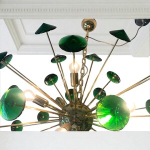 May include: A mid-century modern chandelier with a brass finish and green glass accents. The fixture features multiple arms extending from a central sphere, each holding a green glass orb or disc. The design includes exposed light bulbs.