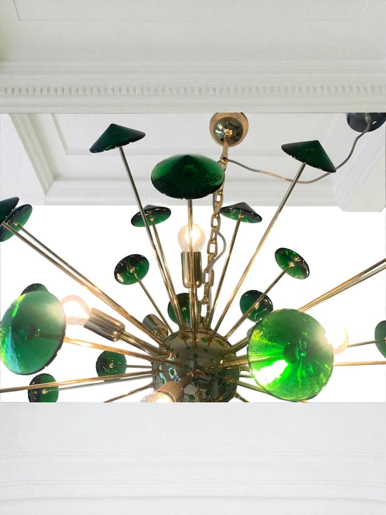 May include: A mid-century modern chandelier with a brass finish and green glass accents. The fixture features multiple arms extending from a central sphere, each holding a green glass orb or disc. The design includes exposed light bulbs.