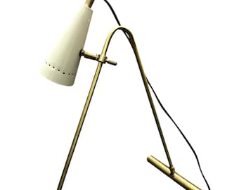 May include: A vintage-style desk lamp with a white conical shade and a brass-colored metal frame. The lamp has a curved arm and a base with a horizontal bar. The shade has small ventilation holes.