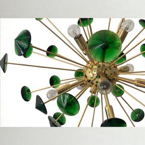 May include: A mid-century modern chandelier with a starburst design. It features gold-toned metal arms extending from a central sphere, adorned with green glass accents and clear light bulbs. The fixture is a striking piece of home decor.