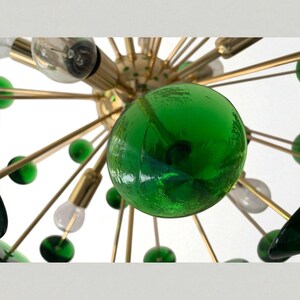 May include: A mid-century modern chandelier with a gold-tone metal frame. The fixture features multiple arms with green glass globes and clear light bulbs. The design is reminiscent of atomic age decor.