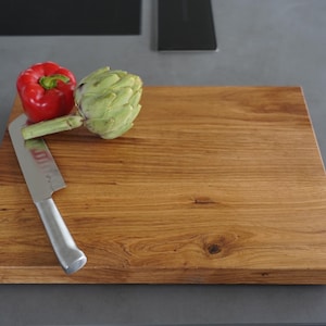 May include: A wooden cutting board with a red bell pepper and an artichoke on top. A silver knife is lying on the board.