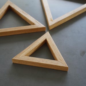 May include: Three wooden triangle frames of varying sizes, arranged on a grey surface. The frames are made of natural wood and have a simple, minimalist design.