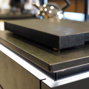 May include: A black granite countertop with a black cutting board on top. The countertop is part of a modern kitchen design.
