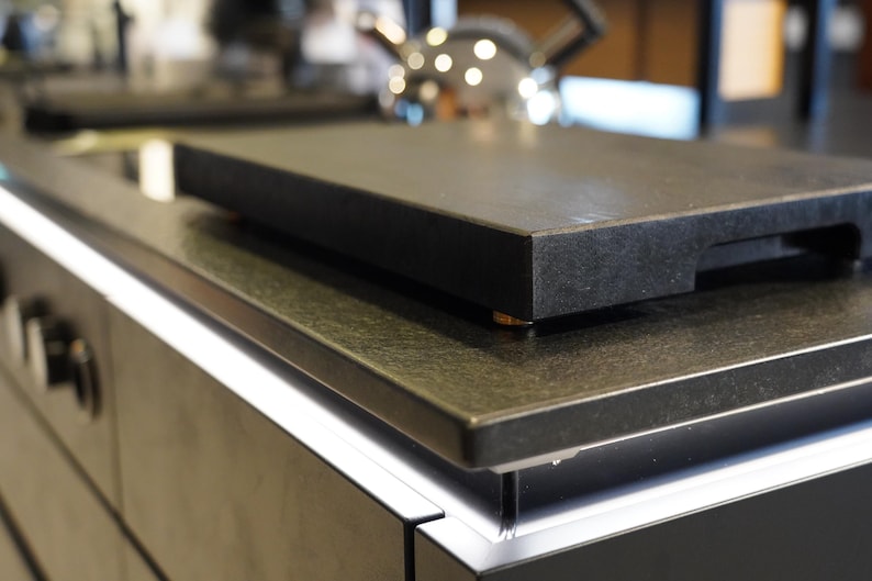 May include: A black granite countertop with a black cutting board on top. The countertop is part of a modern kitchen design.