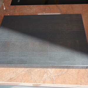May include: A dark gray wooden cutting board with a smooth surface and visible grain patterns. The board is rectangular and has rounded edges.