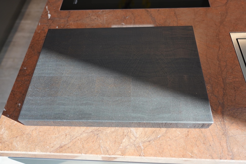 May include: A dark gray wooden cutting board with a smooth surface and visible grain patterns. The board is rectangular and has rounded edges.