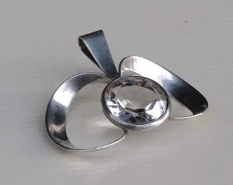 May include: A silver pendant featuring a clear crystal set within three interlocking loops.