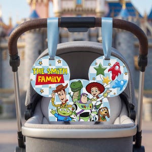 May include: A Mickey-shaped stroller sign featuring a light blue and white checkered background with yellow stars. The text reads THE SMITH FAMILY. The design includes illustrations of Woody, Rex, Buzz Lightyear, Jessie, an alien, and Slinky Dog.