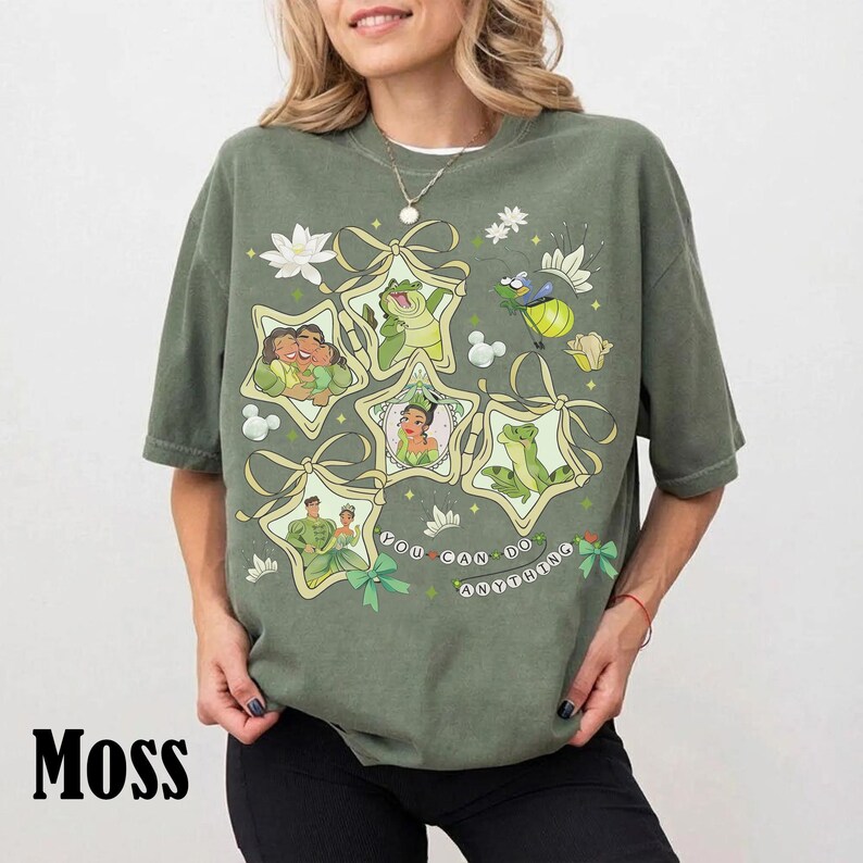 May include: Moss green t-shirt featuring a graphic design with cartoon characters in star-shaped frames. The design includes the text "You Can Do Anything". The shirt has short sleeves and a relaxed fit.