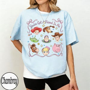 Puede incluir: Camiseta azul claro con un dise&ntilde;o de personajes de Toy Story, incluyendo a Woody y Buzz Lightyear. El dise&ntilde;o presenta el texto "You've Got A Friend In Me" e ilustraciones de varios personajes.