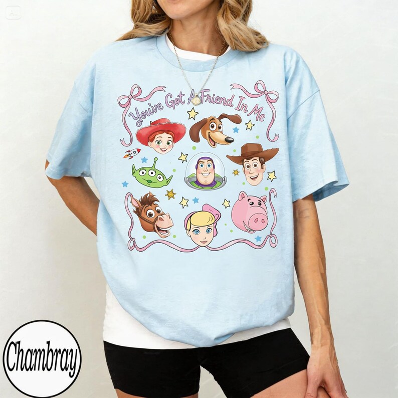 Puede incluir: Camiseta azul claro con un dise&ntilde;o de personajes de Toy Story, incluyendo a Woody y Buzz Lightyear. El dise&ntilde;o presenta el texto "You've Got A Friend In Me" e ilustraciones de varios personajes.