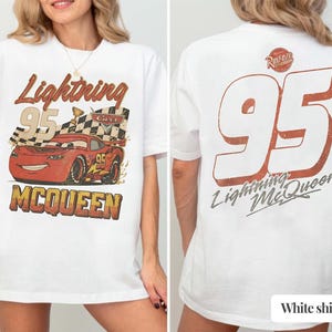 K&ouml;nnte beinhalten: Wei&szlig;es T-Shirt mit einem Front-Grafik von Lightning McQueen aus dem Film Cars, mit dem Text "Lightning McQueen 95". Auf der R&uuml;ckseite des Shirts ist eine gro&szlig;e "95" und der Text "Lightning McQueen" zu sehen.