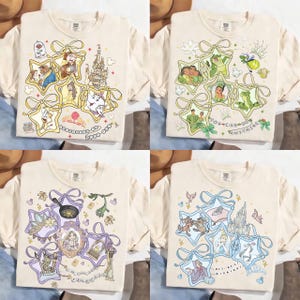 May include: Four cream-colored t-shirts with different Disney-themed designs. Each shirt features a unique arrangement of cartoon characters and elements within star-shaped frames, tied with ribbons. The designs include characters from Beauty and the Beast, Princess and the Frog, Rapunzel, and Cinderella.