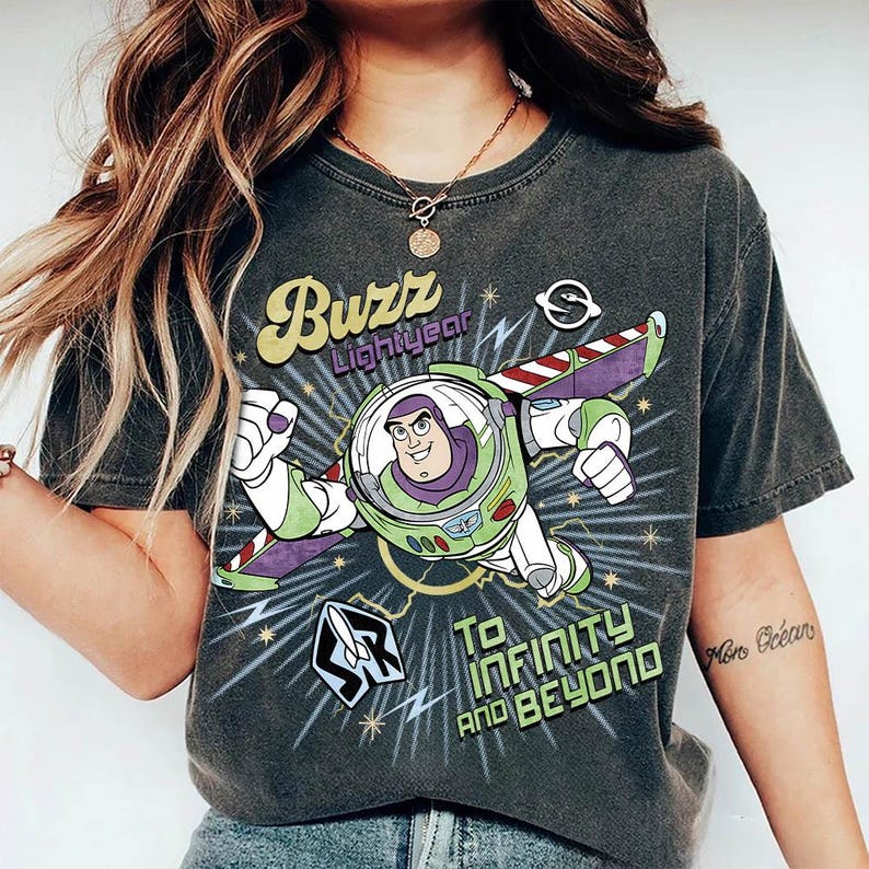 Pu&ograve; includere: Una t-shirt a maniche corte grigio antracite con una grafica di Buzz Lightyear in volo. Il design include il testo "Buzz Lightyear" e "To Infinity and Beyond" in un carattere retr&ograve;, circondato da stelle, fulmini e una piccola icona a forma di razzo.
