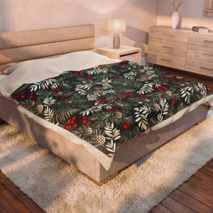 Könnte beinhalten: Eine rechteckige Wohndecke mit dunklem Hintergrund und einem sich wiederholenden Muster aus grünen Kiefernnadeln, hellen Farnblättern, leuchtend roten Beerenclustern und braunen Tannenzapfen, abgerundet durch eine einfarbige cremefarbene Unterseite.