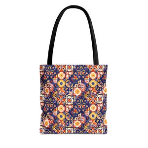 May include: A tote bag featuring a repeating pattern of square tiles in shades of deep blue, bright yellow, orange, and white. The design consists of intricate floral and geometric motifs within each tile. The bag has two solid black shoulder straps.