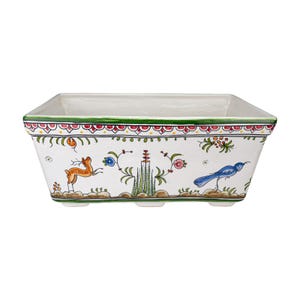 May include: Rectangular white ceramic planter with hand-painted floral and animal designs. The planter features a green and red border, with illustrations of a deer, a blue bird, and floral motifs. The base has three small feet.