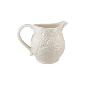 May include: Cream-colored ceramic pitcher with a handle and spout. The pitcher is decorated with a raised relief pattern of grape clusters and leaves. The pitcher has a rounded body and a footed base.