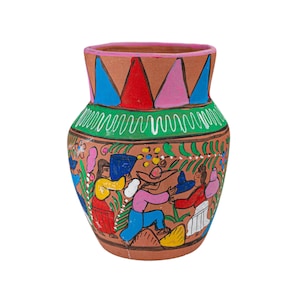 Op de afbeelding: Een terracotta vaas met een handgeschilderde scène van figuren in kleurrijke kleding tussen gebladerte. De hals is versierd met blauwe, rode en roze driehoeken, terwijl een groene band met witte golvende lijnen het bovenlichaam omcirkelt.