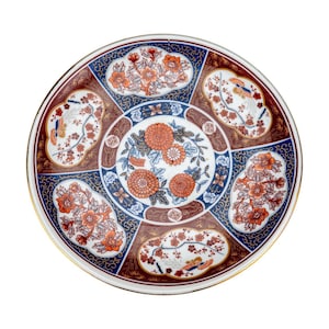 May include: A round, decorative ceramic plate with a gold rim. The plate features a central floral design in orange and blue, surrounded by six sections with floral and bird motifs in orange, white, and brown. The background is a mix of blue and brown.