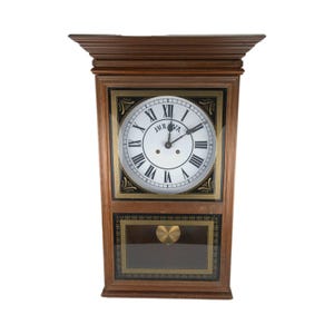 May include: A rectangular wooden wall clock with a white face, black Roman numerals, and the brand name "Bulova". The clock has a decorative gold and black border and a pendulum window.
