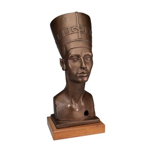 Op de afbeelding: Bronzen buste van Nefertiti, met een hoge hoofdtooi en gedetailleerde gravures. De sculptuur heeft een gladde, verouderde afwerking en is gemonteerd op een rechthoekige houten basis. Een representatie van oude Egyptische kunst.
