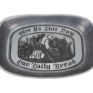 May include: An oval-shaped silver-toned metal tray featuring an embossed scene of a person harvesting wheat in a field. The text "Give Us This Day" is arched above the scene, and "Our Daily Bread" is inscribed in a decorative font below it.