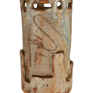 Könnte beinhalten: Eine zylindrische Keramikvase mit einer strukturierten, gesprenkelten Oberfläche in Braun-, Beige- und blaugrünen Farbtönen. Die Vase hat rechteckige Aussparungen in der Nähe der Oberseite und eingravierte lineare Designs. Der Sockel hat einen dunkleren, rotbraunen Farbton.