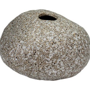 Könnte beinhalten: Eine gesprenkelte, grau-steinartige Vase mit runder Form und einer einzigen Öffnung oben. Die Vase hat eine raue, strukturierte Oberfläche mit kleinen dunklen Punkten, die eine natürliche, organische Ästhetik erzeugt. Die neutrale Farbpalette macht sie für verschiedene Einrichtungsstile geeignet.