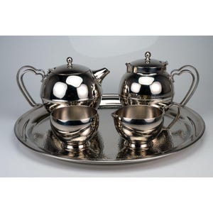 May include: A polished silver-tone tea set consisting of a teapot, a lidded sugar bowl, a creamer, and a matching round serving tray. Each piece features a smooth, reflective finish and curved handles, arranged together on the circular tray.