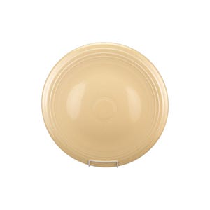 Puede incluir: Un plato redondo de color crema con detalles concéntricos acanalados. El plato está hecho de cerámica y se exhibe sobre un soporte de metal blanco. El plato tiene un acabado liso y brillante y un diseño simple y clásico.