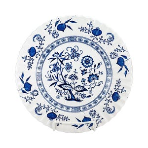 May include: White ceramic plate with a blue floral design. The plate features a scalloped edge and a central motif of stylized flowers and foliage. The blue and white color scheme gives the plate a classic, vintage aesthetic.