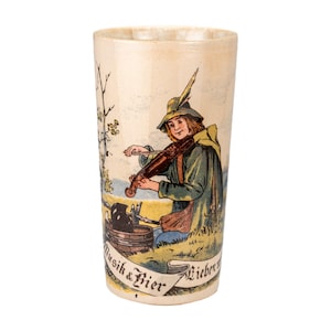 May include: A vintage ceramic beer stein with a painted illustration of a musician playing a violin. The musician is wearing a green coat and hat. The stein has the words "Musik & Bier" on it.