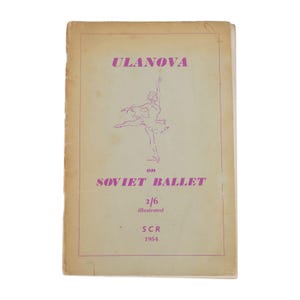 Może przedstawiać: Vintage okładka książki z tytułem "ULANOVA" w fioletowych literach nad ilustracją baletnicy. Tekst "on SOVIET BALLET" znajduje się pod ilustracją. Okładka zawiera również "2/6 illustrated" i "SCR 1954". Tło jest beżowe.