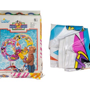 May include: A 24-inch Mickey and Pals inflatable swim ring in its original packaging. The packaging features a graphic of the swim ring with colorful cartoon characters, and the deflated swim ring is shown folded next to the box.