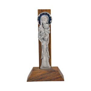 Könnte beinhalten: Religiöse Figur aus silberfarbenem Metall, die eine Frau mit einem Kind darstellt. Auf einem Holzsockel und einer Holzrückwand montiert. Die Frau hat einen blauen Heiligenschein. Der Sockel und die Rückwand sind dunkelbraun.