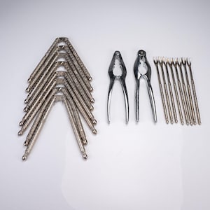 May include: A set of silver-toned metal kitchen tools including six nutcrackers with textured handles, two smooth nutcrackers with serrated inner grips, and eight slender two-pronged seafood forks with matching textured handles.