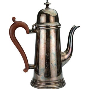 Puede incluir: Una cafetera plateada vintage con un asa de madera. La cafetera tiene un cuerpo alto y cilíndrico con un pico curvo y una tapa abovedada. El asa es de color marrón oscuro y la cafetera tiene una superficie brillante y reflectante.