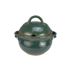 May include: A handcrafted, dark green ceramic soup tureen with a matching lid. The tureen has a rounded body, two side handles, and a loop handle on the lid. The lid features a small opening for a ladle. The rim has a brown accent.