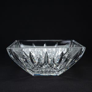 May include: A clear, square glass bowl featuring a faceted, starburst-like cut pattern on its exterior walls. The thick glass construction creates a reflective surface with sharp, geometric edges and a smooth, transparent finish throughout.