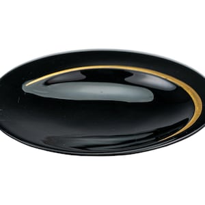 May include: A black oval dish with a gold trim. The dish has a smooth, glossy surface and a shallow, curved interior. The gold trim provides a contrasting accent to the black, creating a simple yet elegant design.