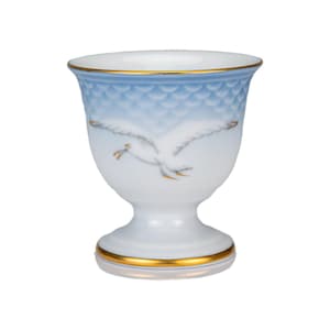 Op de afbeelding: Een wit en blauw porseleinen eierdopje met een gouden rand en voet. De beker heeft een handgeschilderd ontwerp van een vliegende zeemeeuw. De bovenkant van de beker heeft een blauw, gestructureerd patroon.